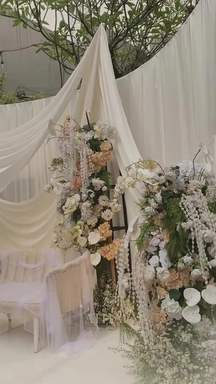 Rangkaian bunga putih dan peach dengan juntaian manik di depan drape kain krem