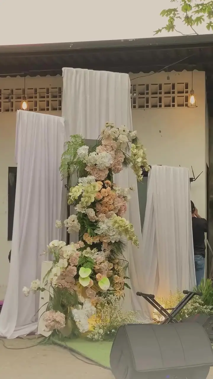 Standing flower peach dan putih di antara panel kain putih dengan lampu sorot lantai